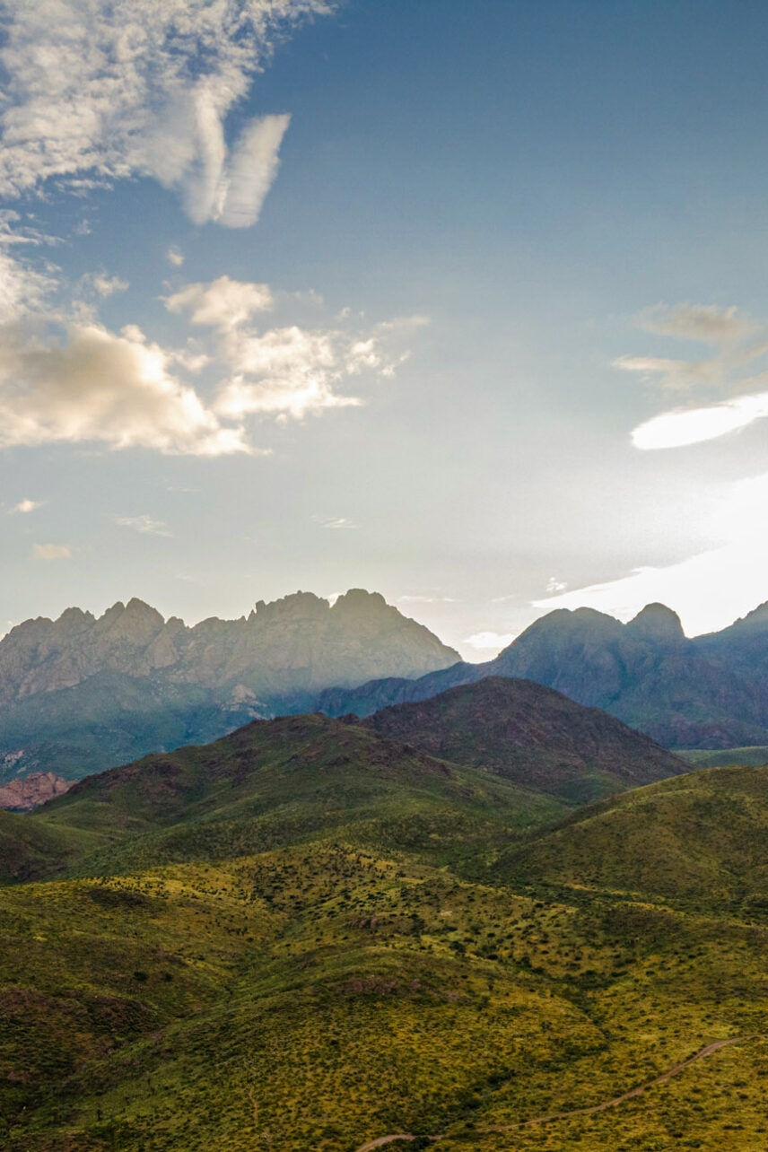 Mobile sized image of The Organ Mountains in the distance with green rolling hills in the foreground