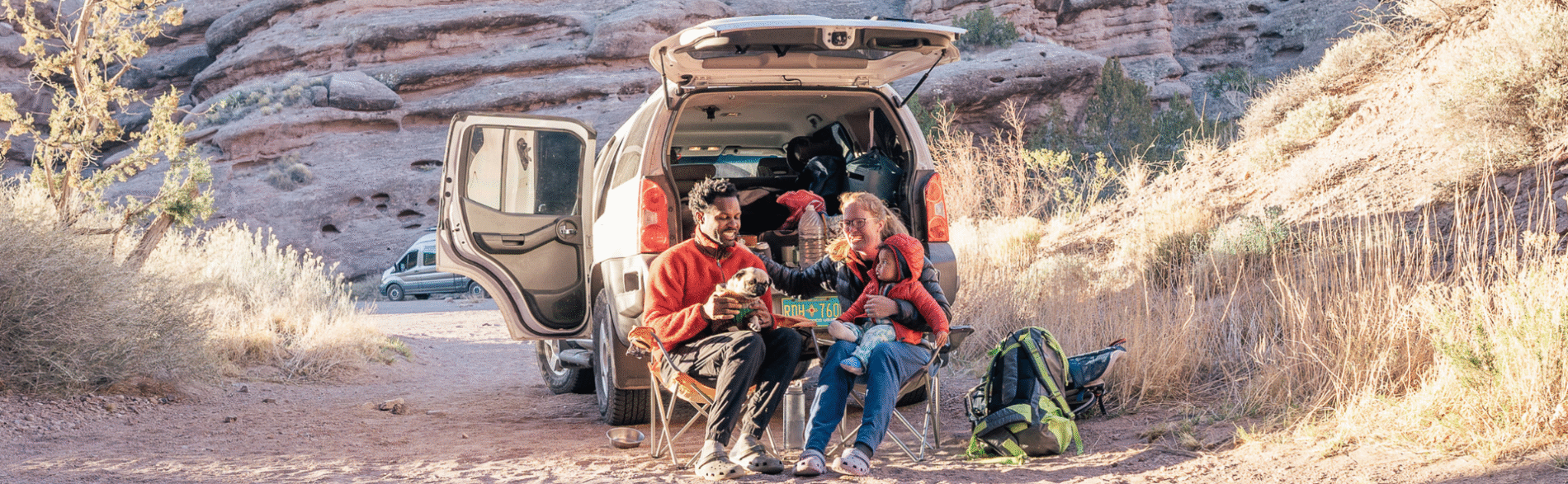 A multiracial family, mom, dad, and son, sitting on camp chairs behind their van enjoying the outdoors
