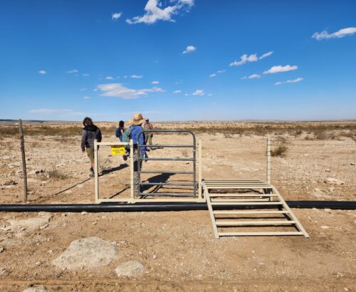 A fence with a newly installed cattle guard and pedestrian gate in the desert.