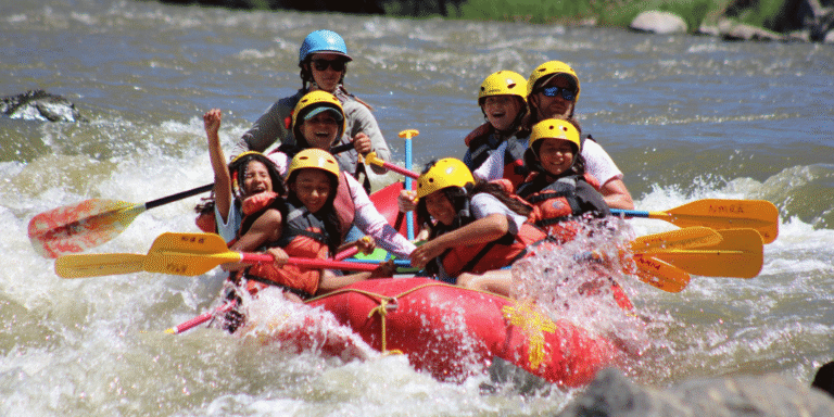 a group of kids white water rafting through a large rapid