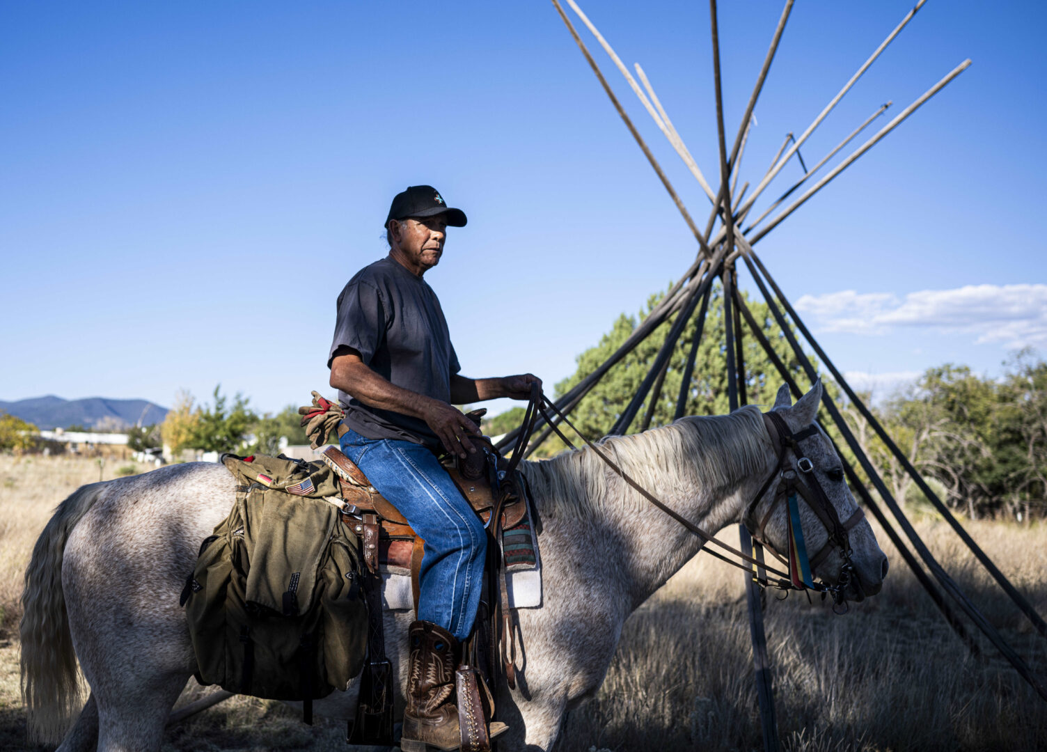 An Apache man on a horse with a teepee stand in the bacgkround