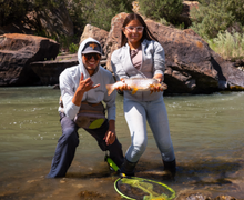 young woman holding a large fish while standing in the river looking excited