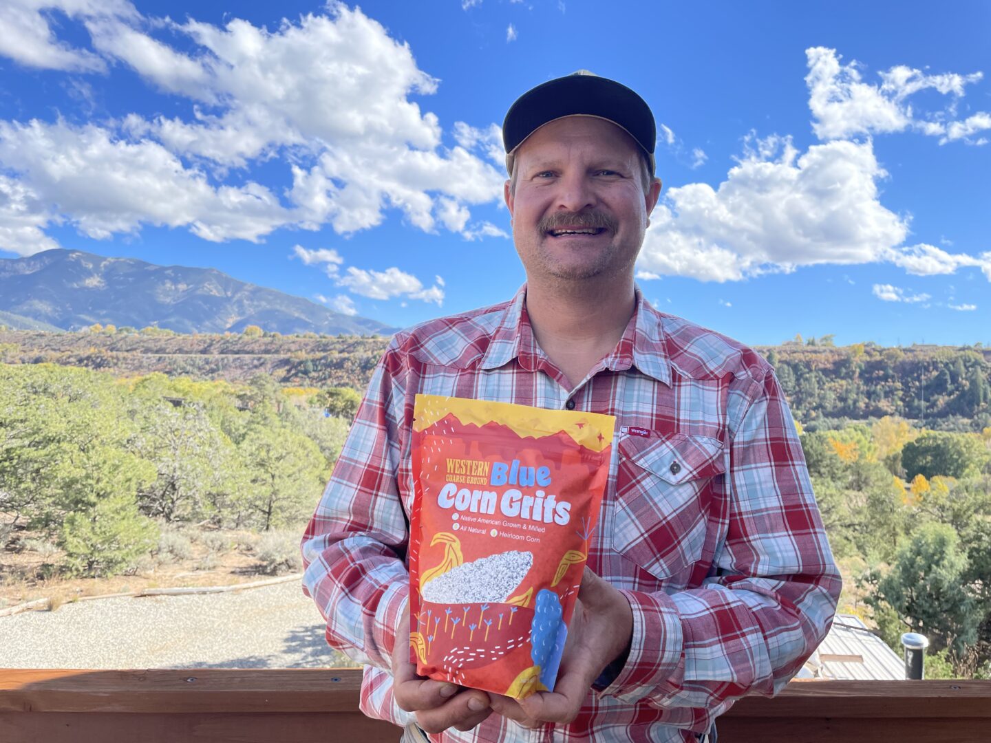 A man in flannel smiling and proudly displaying a bag of his blue corn grits.