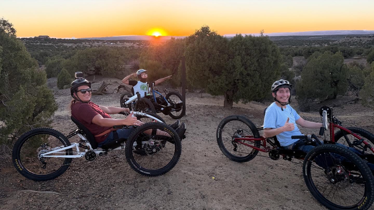 three teenagers in recumbent adaptive mountain bikes on a trail at sunset