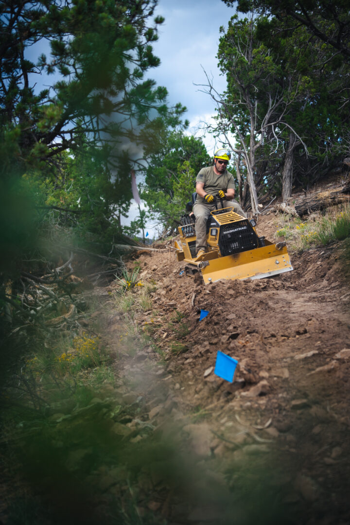 A man driving a mini bulldozer clearing a new section of dirt trail in a forest