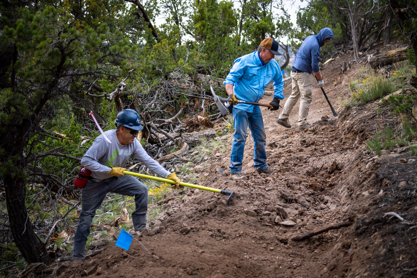 Three men swinging trail tools and building a fresh section of dirt trail