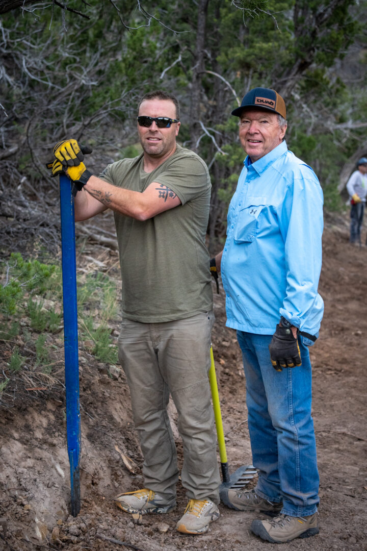 Two men, a father and son, pose with trail tools while working on building a trail