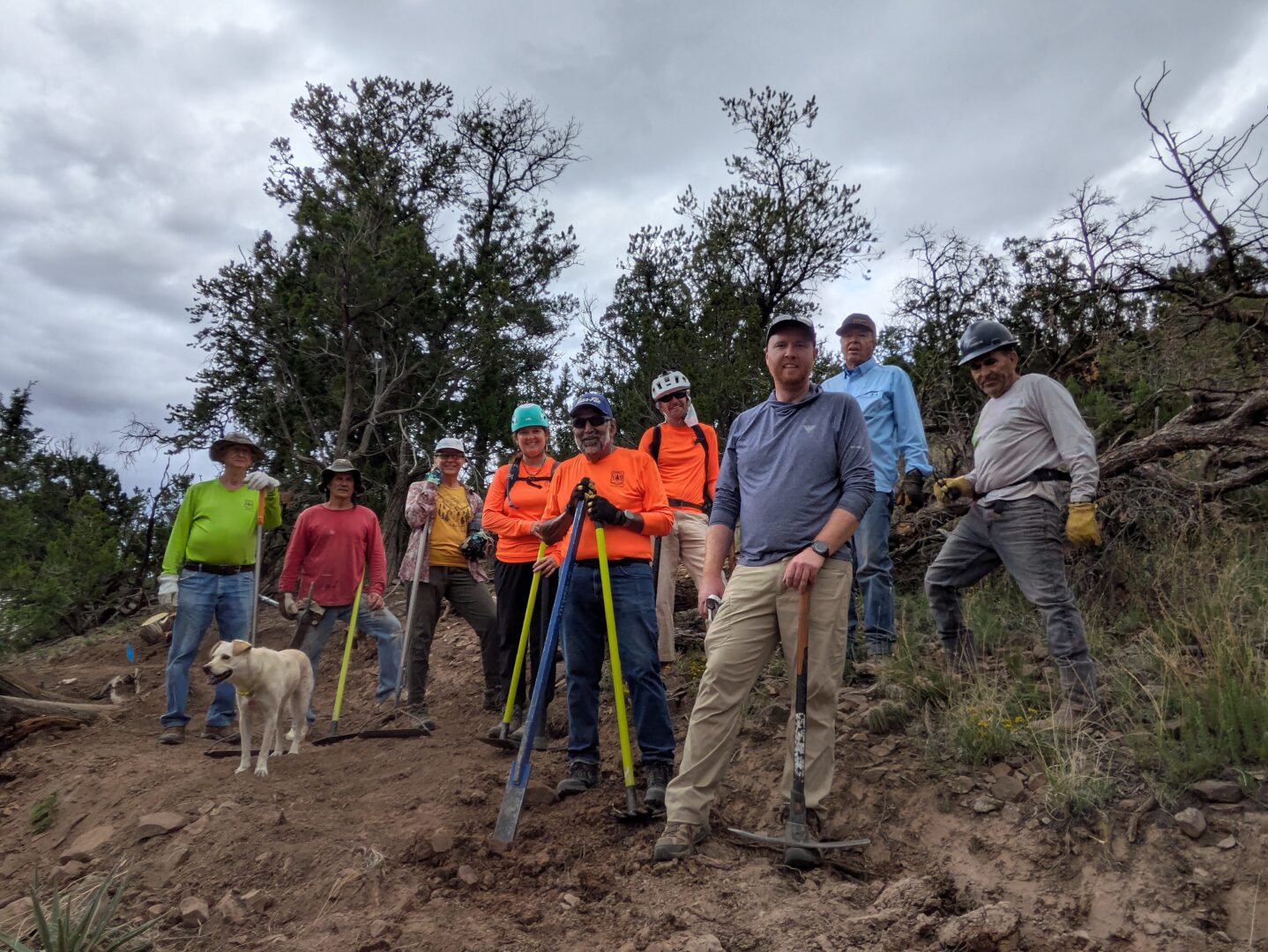 Group of trail workers holding tools and posing on a section of freshly built trail on a cloudy day