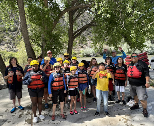 Group of kids wearing life jackets and safety helmets posing before a whitewater rafting trip