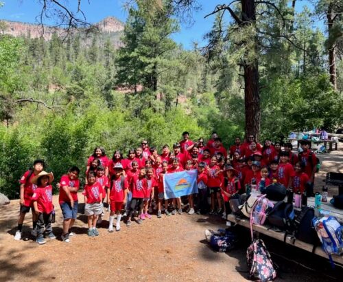 Large group of kids wearing maching red shirts holding an outdoor equity fund flag in the wilderness