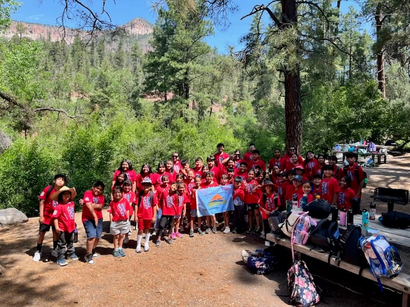 Large group of children wearing matching red shirts holding an outdoor equity fund flag in the wilderness