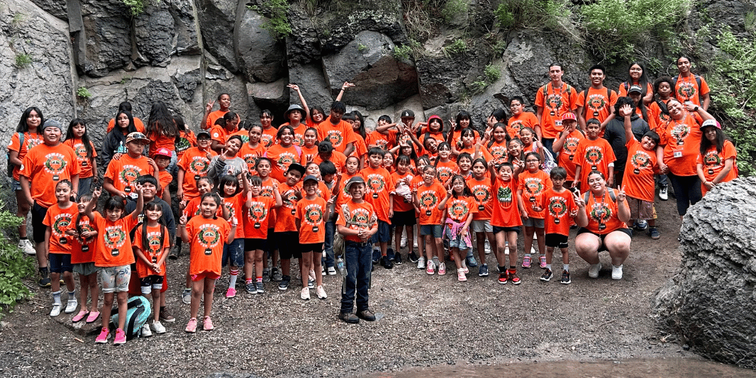 Large group of children wearing matching orange shirts smiling and posing in front of a rocky formation