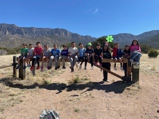 Group pf youth sitting on a fence in the desert with mountains in the background