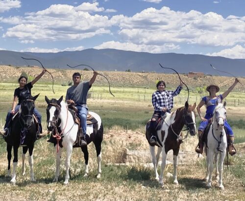 4 teens on horses holding bows in front of a mountain