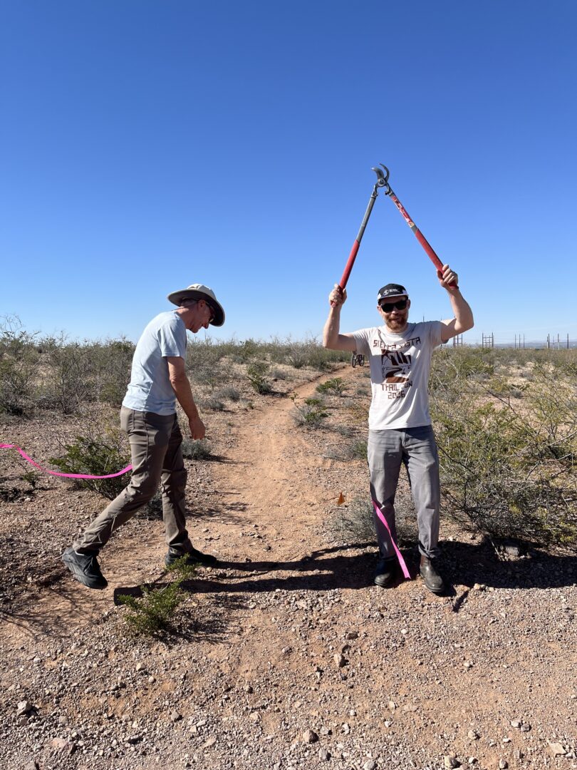 A man holding up loppers after cutting a ribbon at a trailhead in the desert