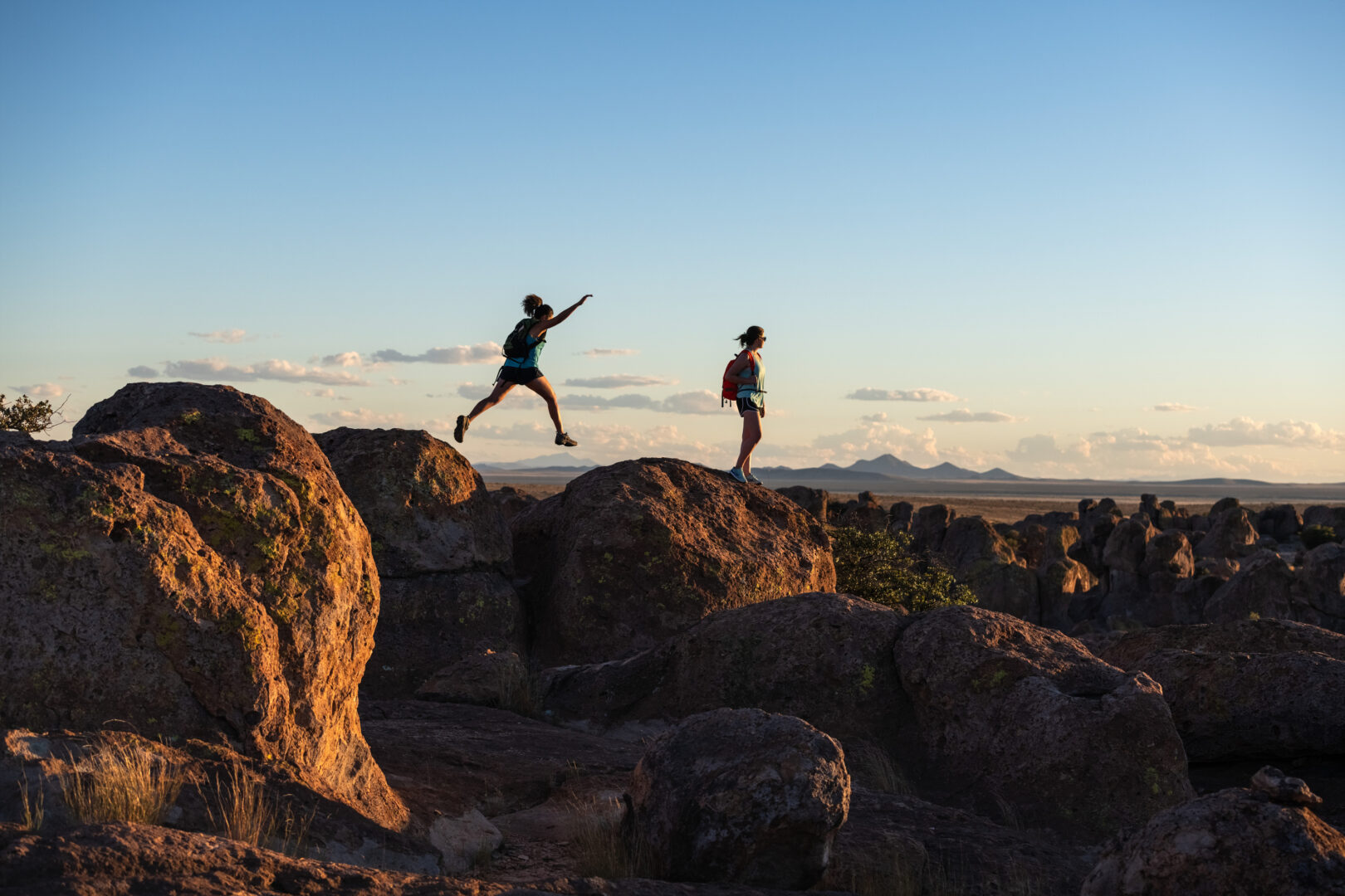 Silhouette of two kids jumping across large rocks