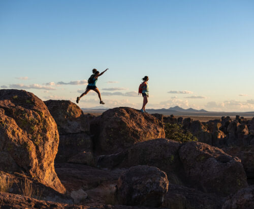 Silhouette of two kids jumping across large rocks