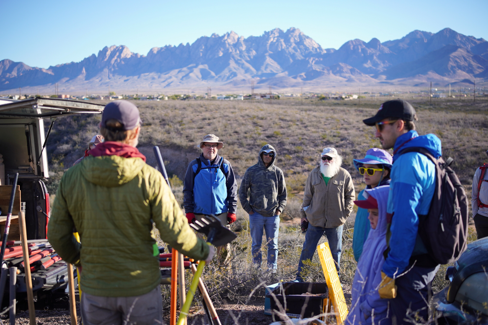 A group of volunteers standing around trail tools with the Organ Mountains in the background