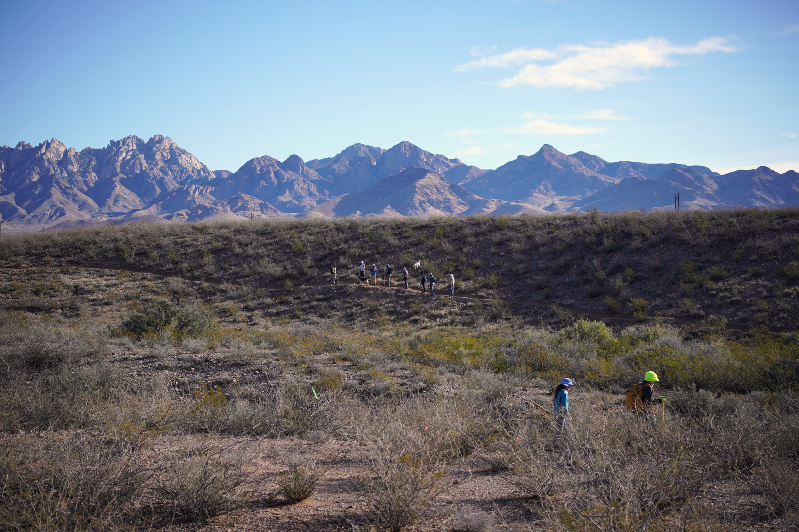 Trail workers walking along a trail in the distance with the organ mountains behind them