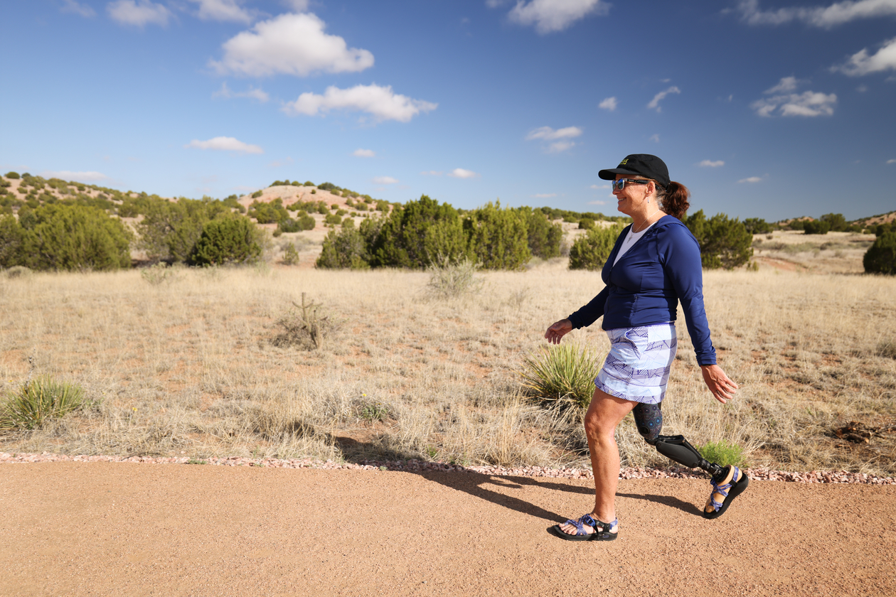 A woman using a prosthetic leg smiles as she hikes a flat desert trail