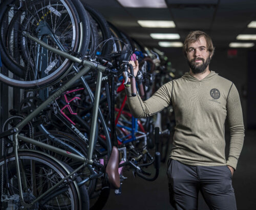 Man standing in a bike shop posing next to a wall of bikes