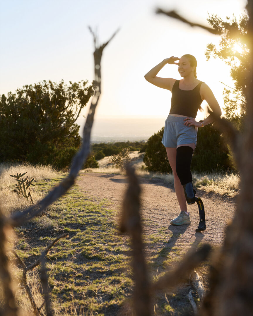 A woman standing on a desert trail wearing a running blade and smiling as she looks into the distance