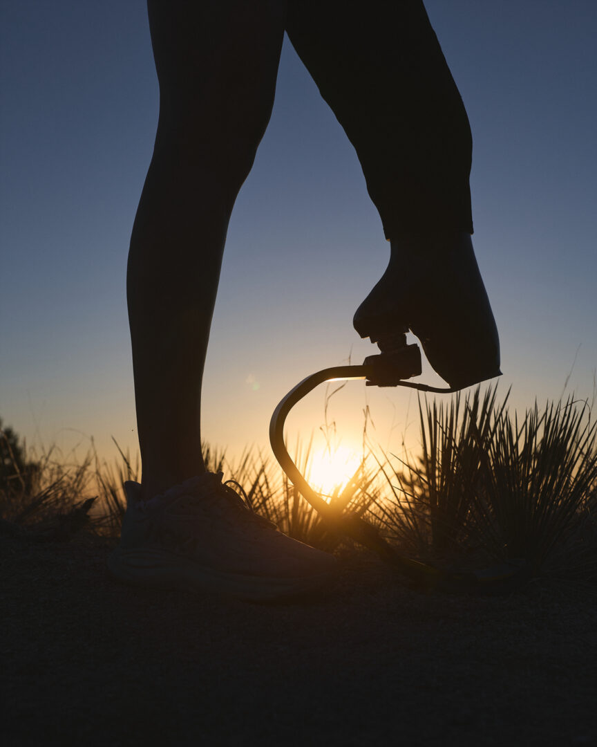 Silhouette of a woman standing wearing a running blade on one leg at sunset in the desert