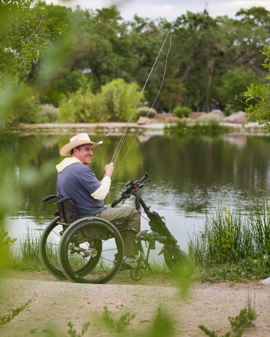 A man fishing and smiling in a wheelchair with a firefly attachment to help him get around on unpaved surfaces