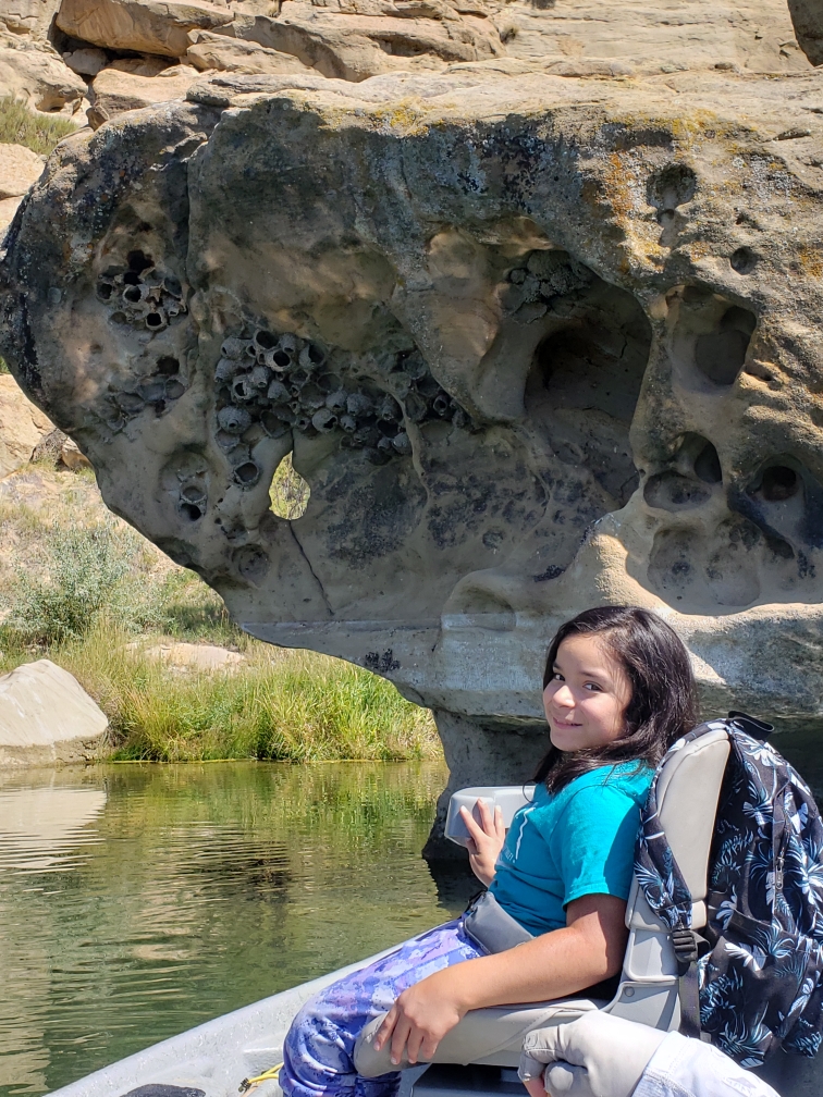 A child sitting on an adaptive-friendly boat smiling at the camera with a featured rocky outcrop in the background