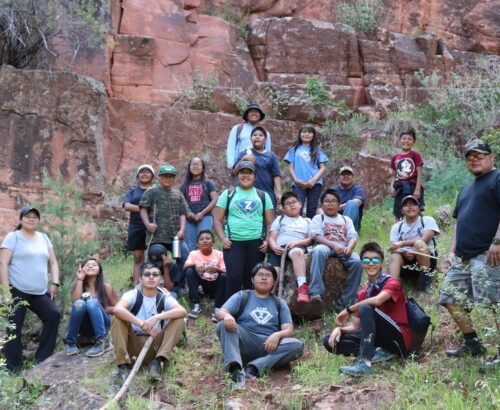 Group of children posing in front of a large red rock wall