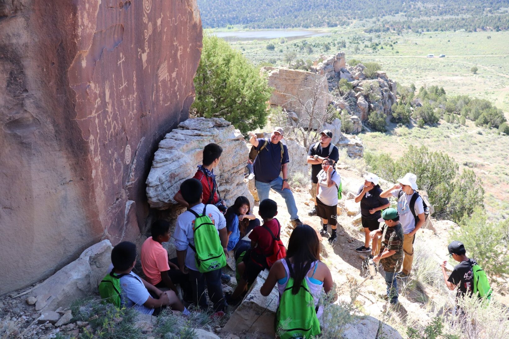 A group of children on a tour looking at petroglyphs up close on a red rock wall