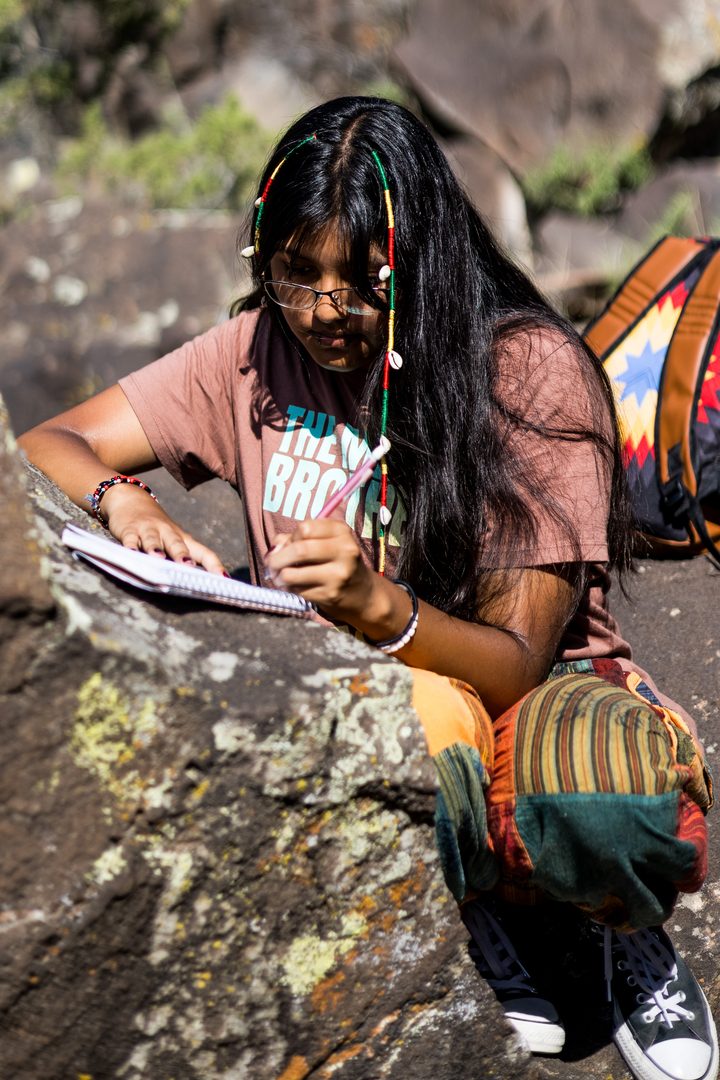 A young person leaning on a rock jotting down notes in a notebook