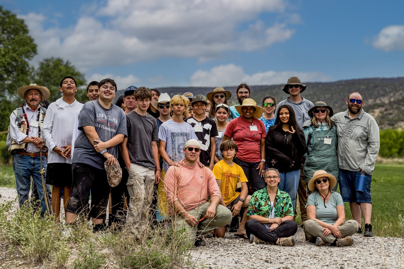 Two dozen students pose and smile in a field with a mesa behind them