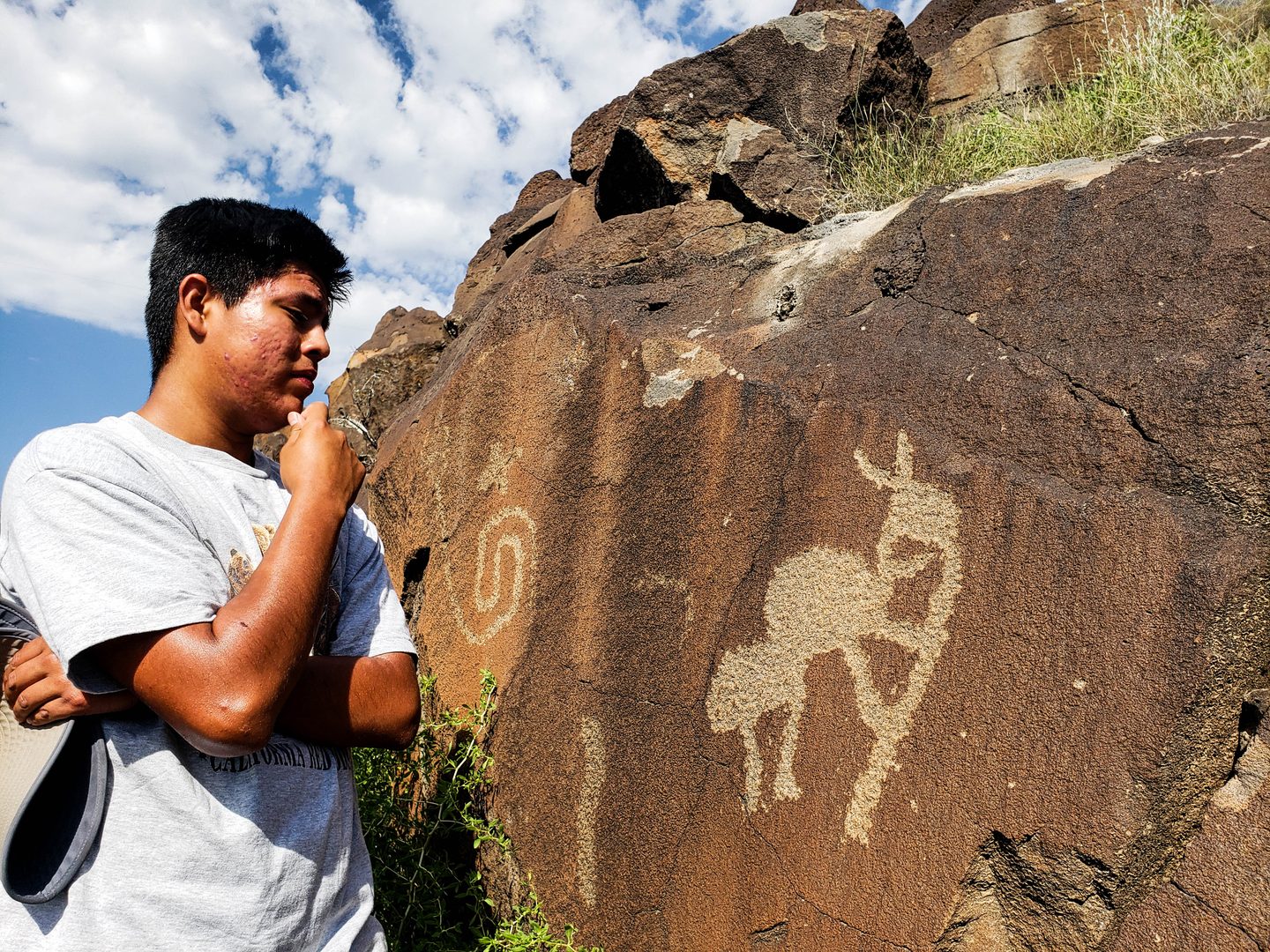 A young man looking at a petroglyph with a hand on his chin deep in thought