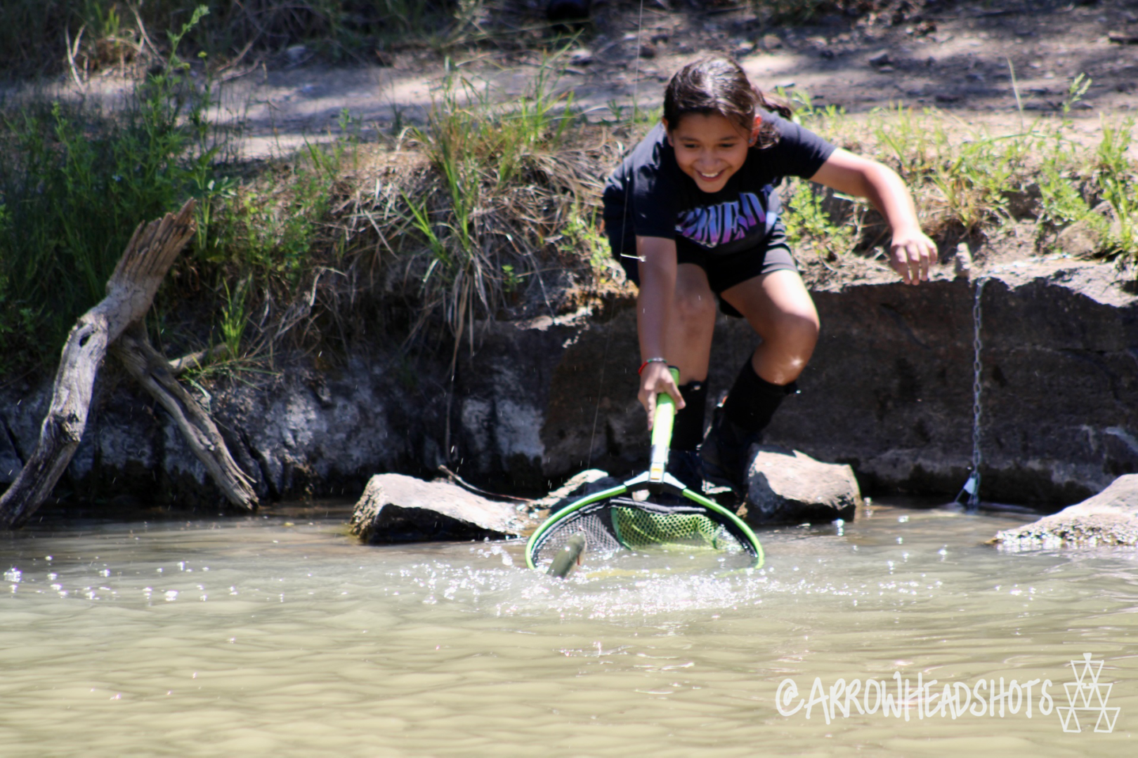 Child excitedly netting a fish from a river bank