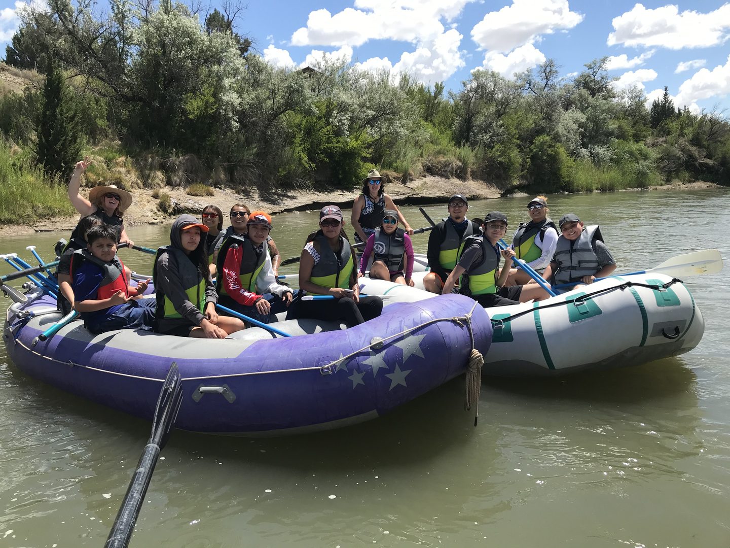 Two groups of river rafters sitting next to each other on large rafts on a sunny day